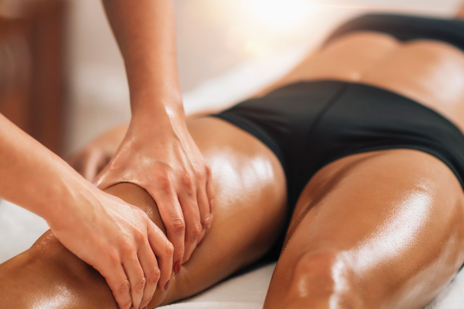 Persona recibiendo un masaje de piernas, tumbada. Masajea el muslo con aceite.