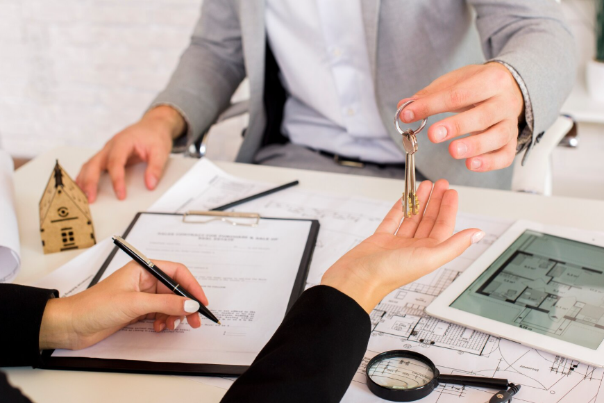 Intercambio de llaves de casa sobre documentos y planos en un escritorio.