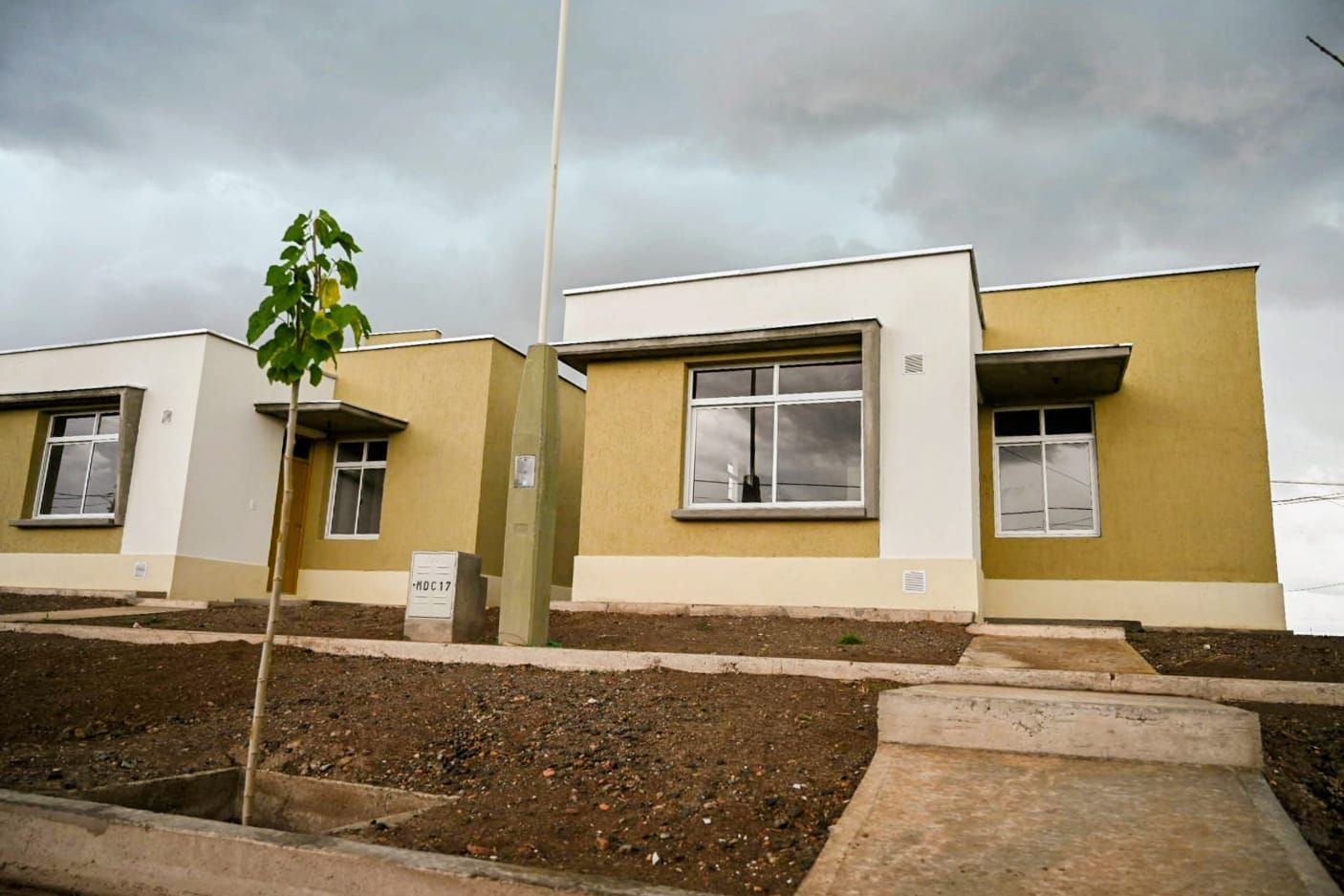 Hilera de pequeñas casas modernas con fachadas beige y blancas bajo un cielo nublado.
