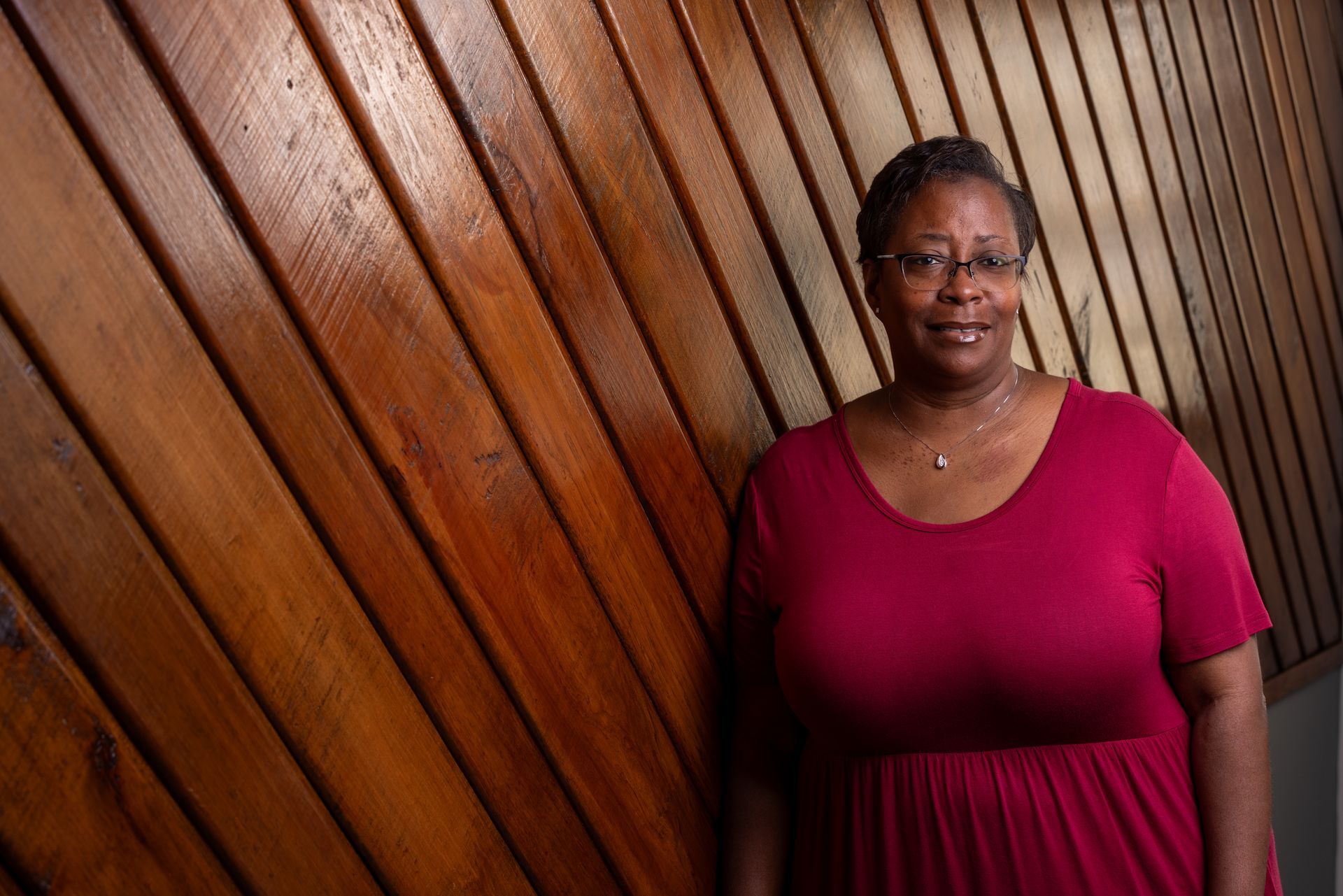 A woman in a red dress is standing in front of a wooden wall.