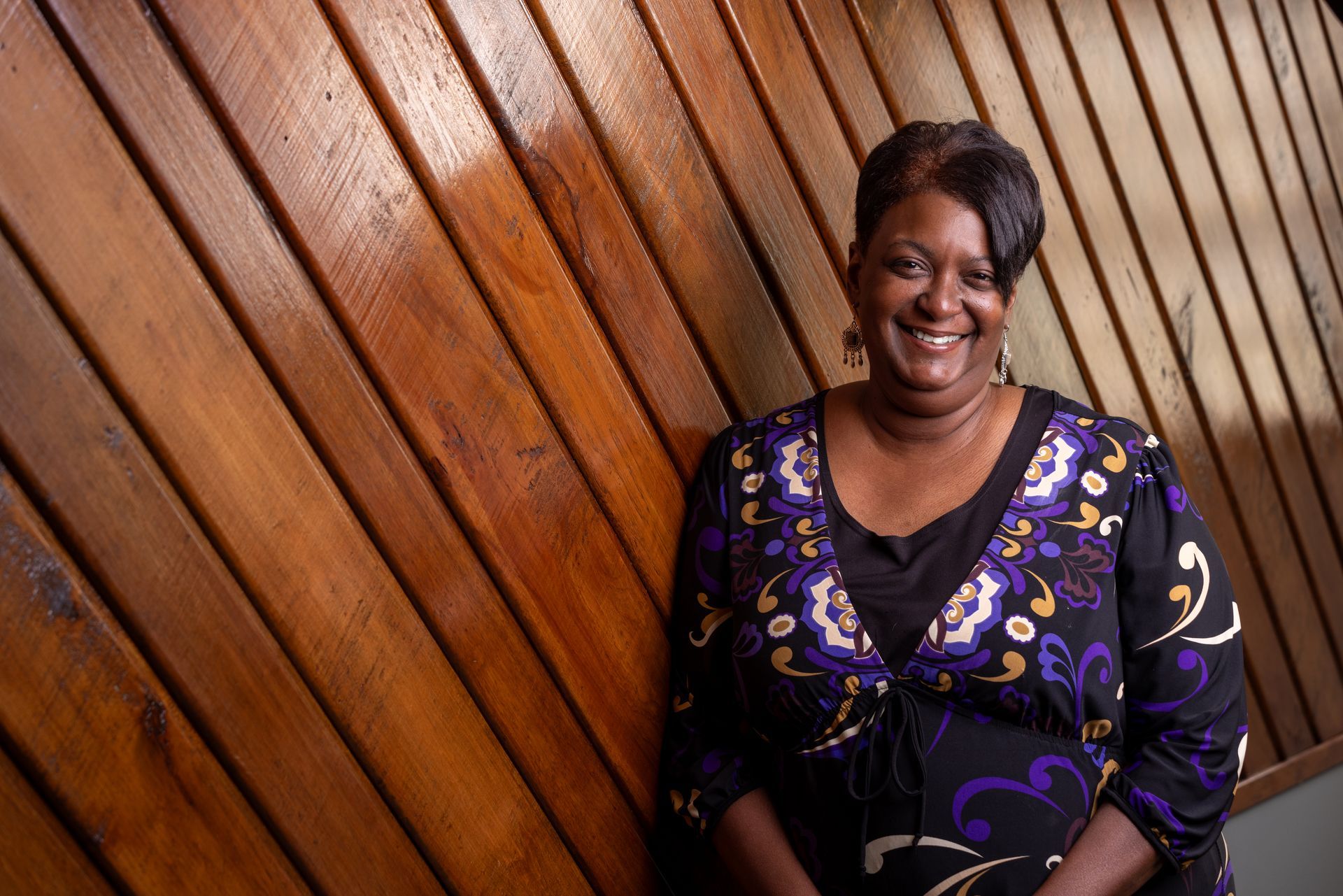 A woman in a purple dress is standing in front of a wooden wall.