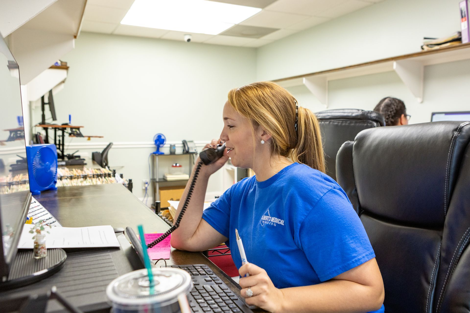 A woman is sitting at a desk talking on a phone.