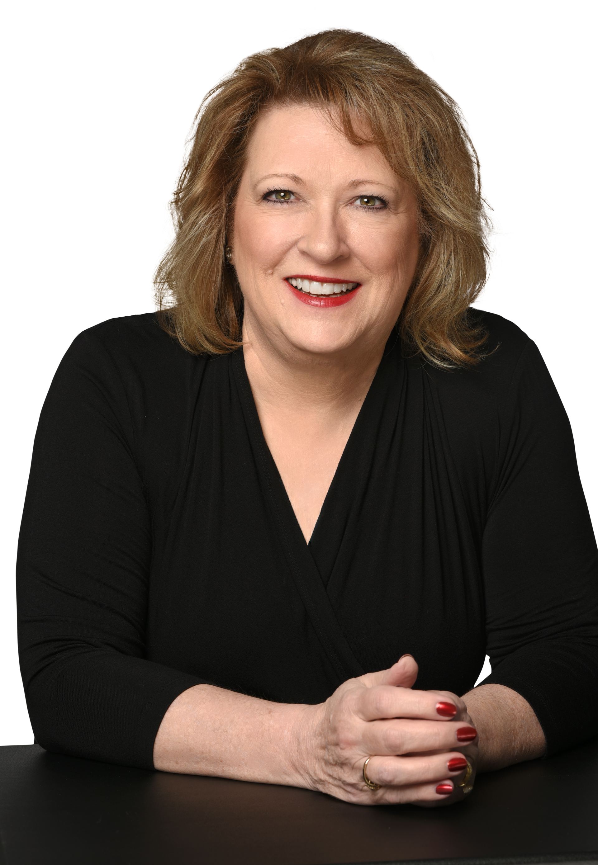 A woman is sitting at a table with her hands folded and smiling.