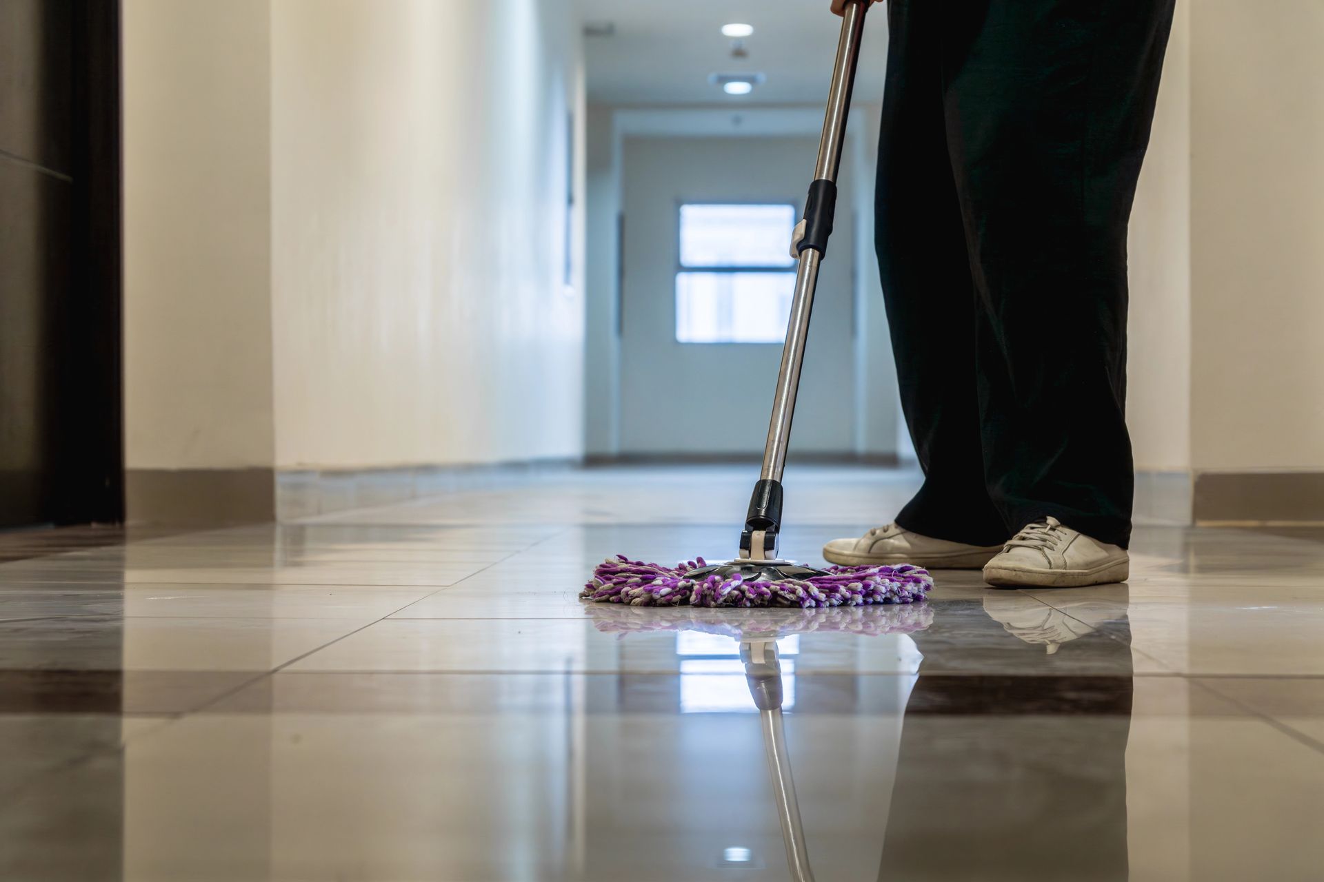 Una persona está fregando el suelo de un pasillo con un trapeador.
