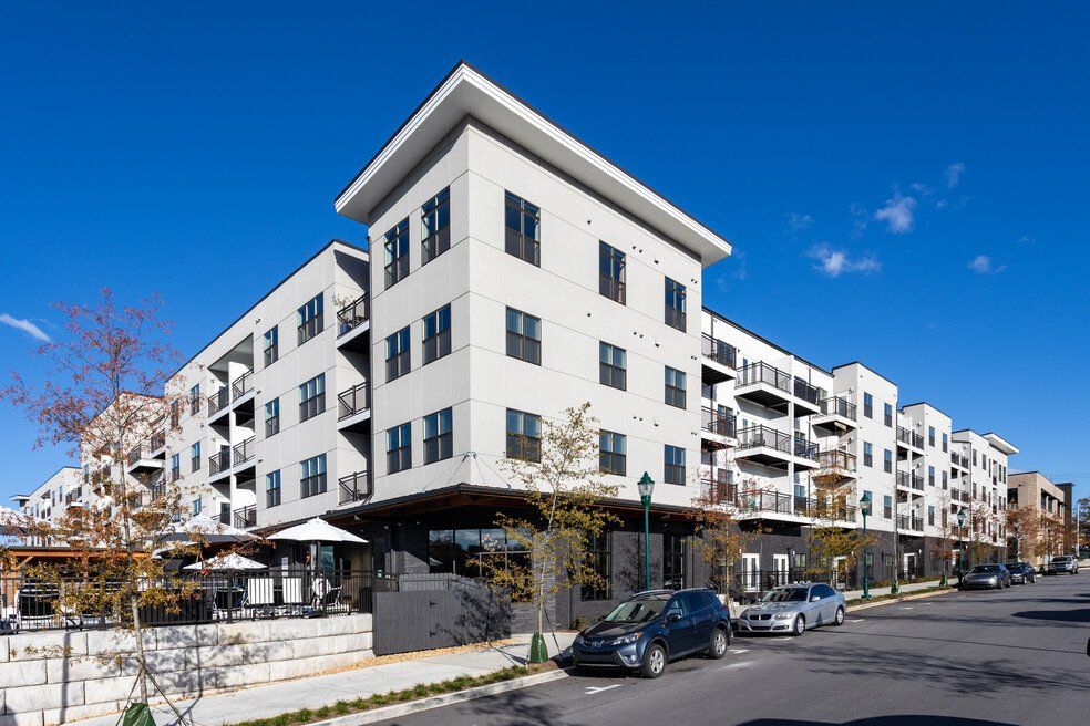 A large apartment building with cars parked in front of it on a sunny day.