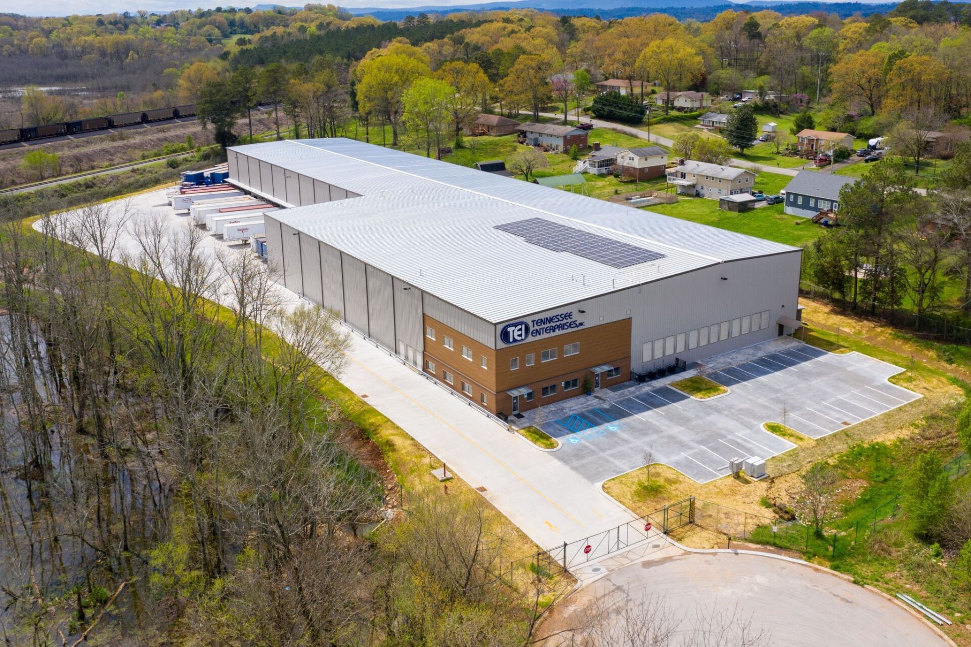 An aerial view of a large building with solar panels on the roof surrounded by trees.
