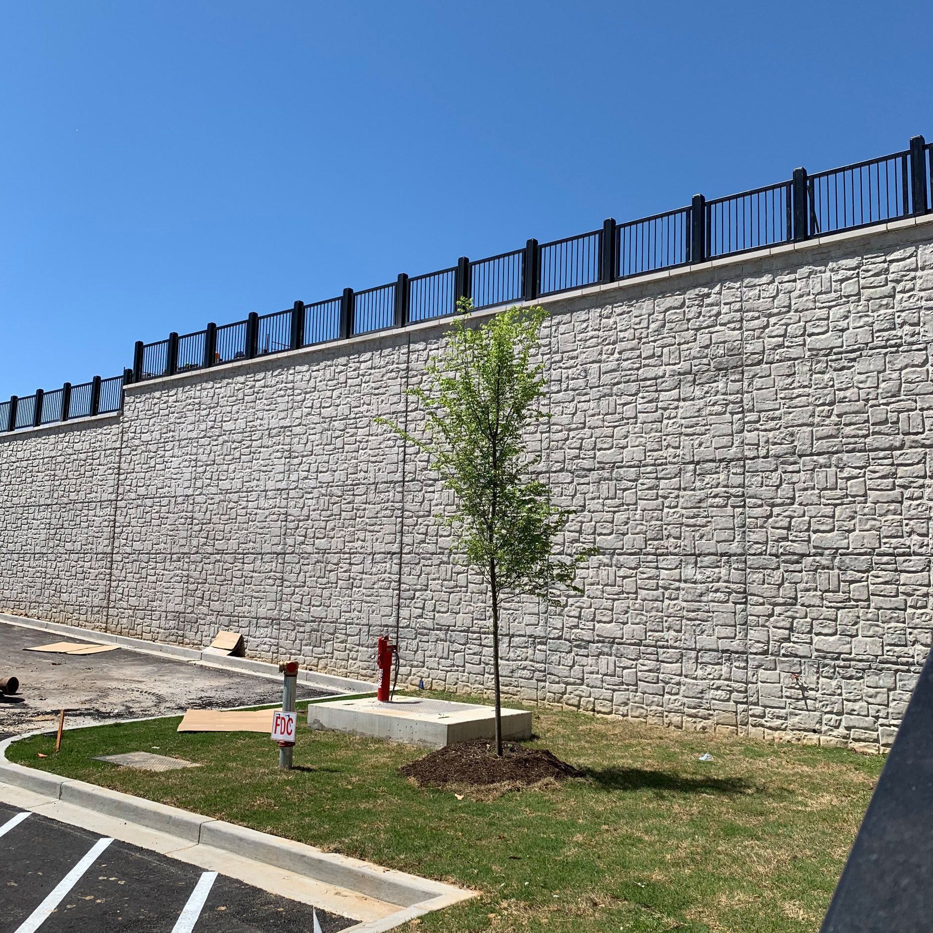 A large stone wall with a fence and a tree in front of it.