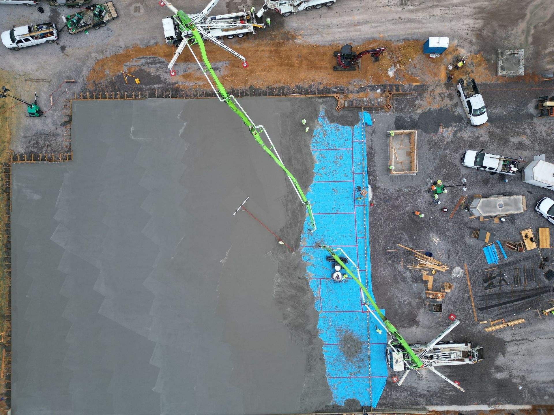 An aerial view of a construction site with a green crane pumping concrete.