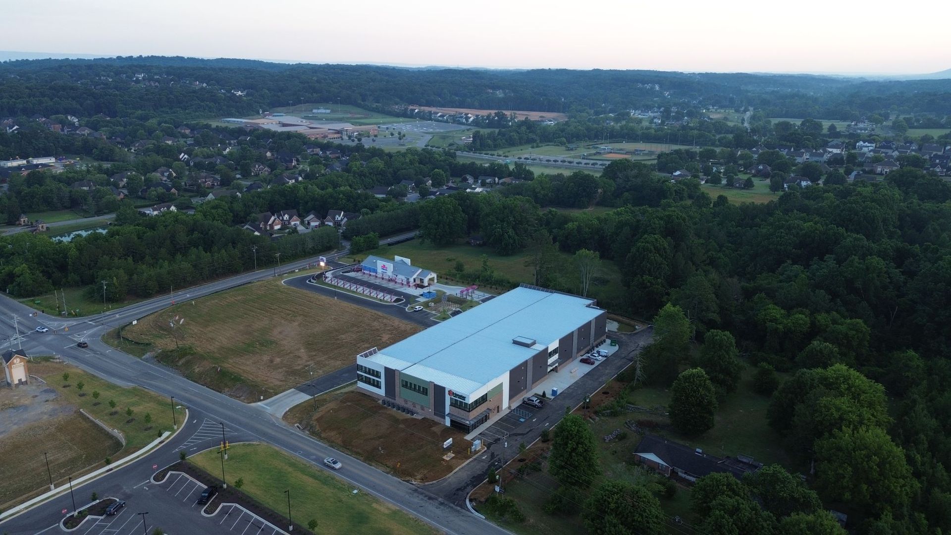 An aerial view of a large building surrounded by trees and a road.