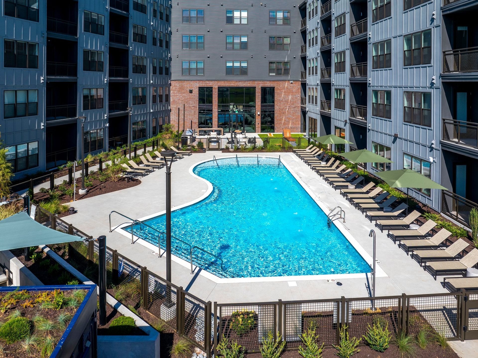 A large swimming pool surrounded by chairs and umbrellas in front of a building.