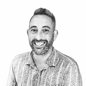 A man with a beard is smiling in a black and white photo.