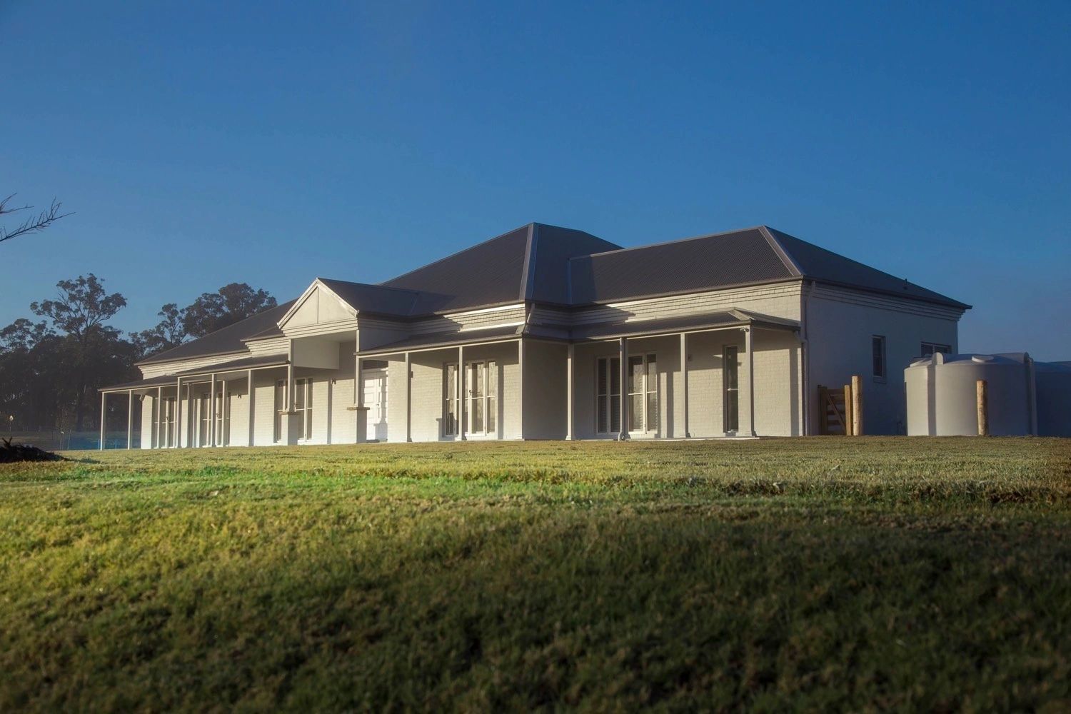 A large white house is sitting in the middle of a grassy field.
