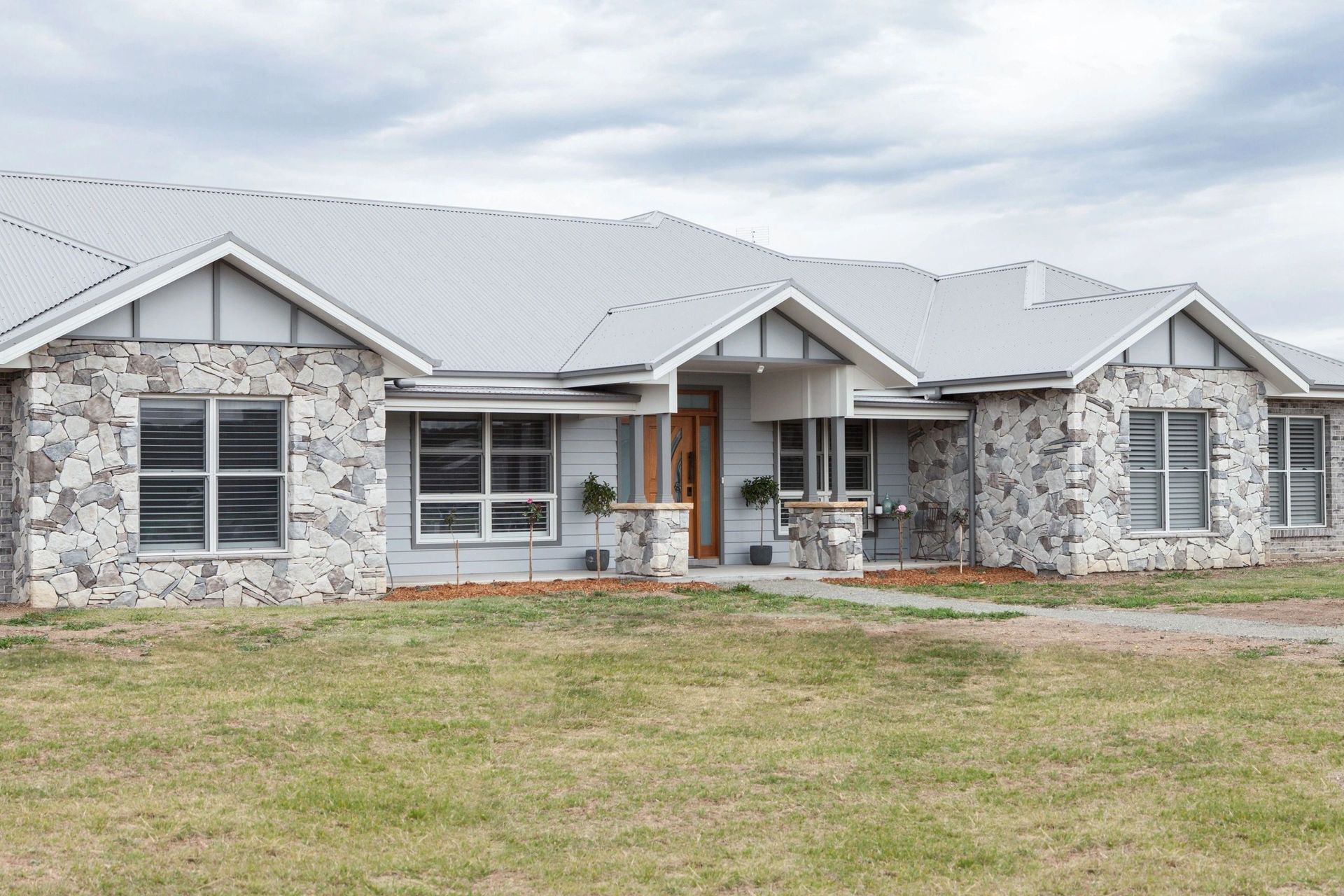 A large house with a stone facade and a white roof is sitting on top of a lush green field.