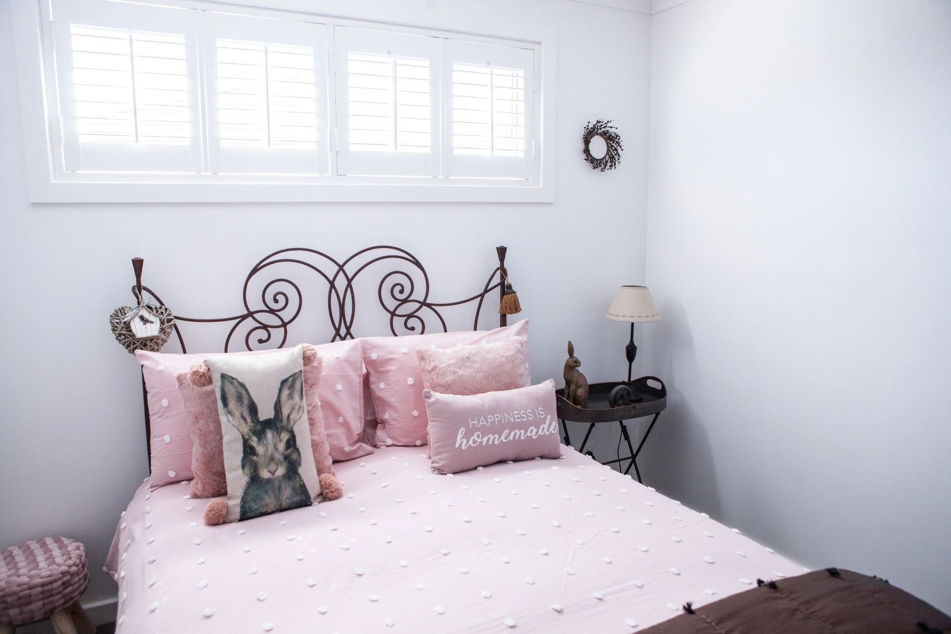 A bed with pink sheets and pillows in a bedroom with a window.