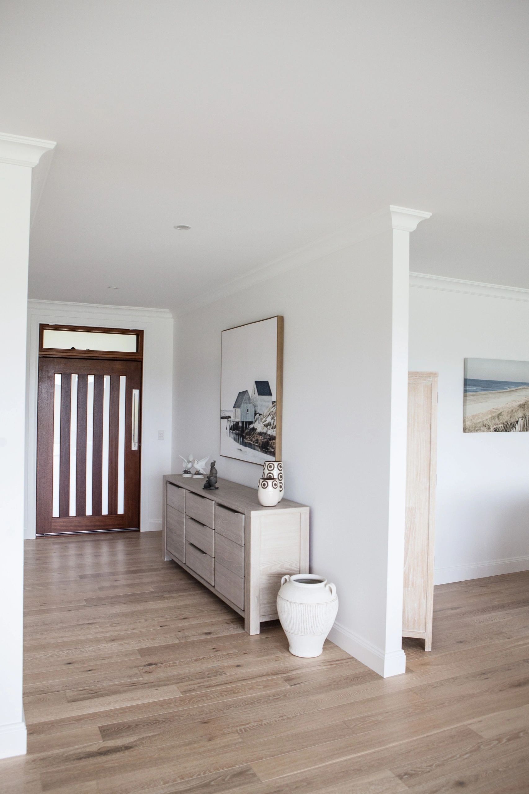 A living room with hardwood floors , a dresser , a vase and a painting on the wall.