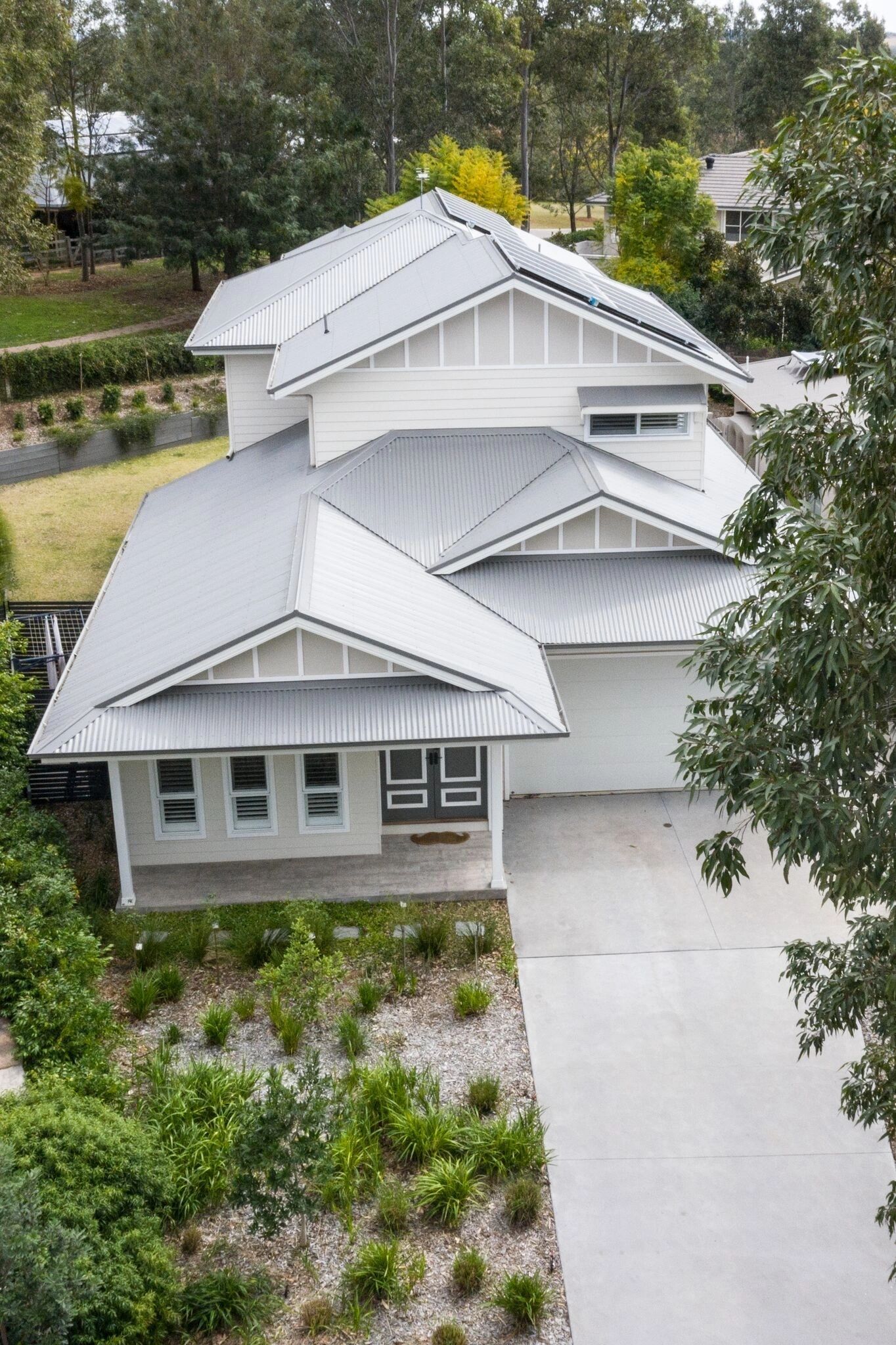 An aerial view of a white house with a gray roof surrounded by trees.