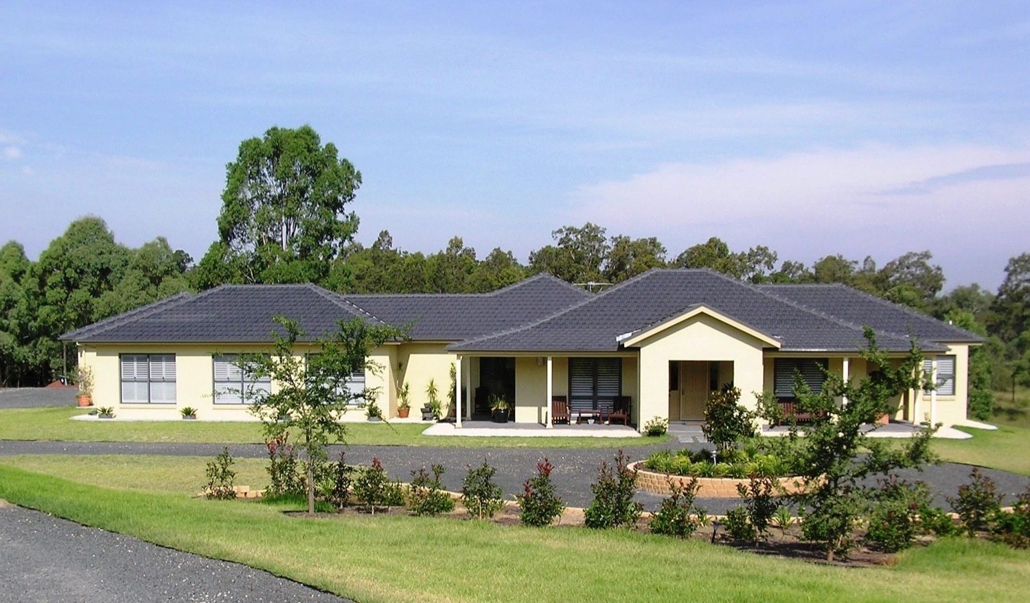 A large house with a black roof sits in the middle of a lush green field