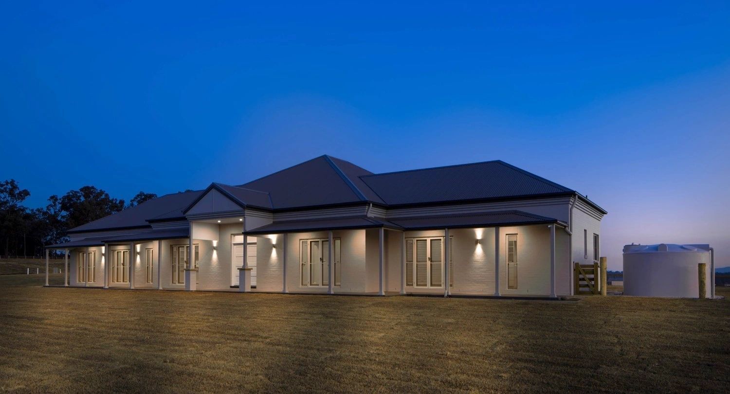 A large white house is sitting on top of a grassy hill at night.