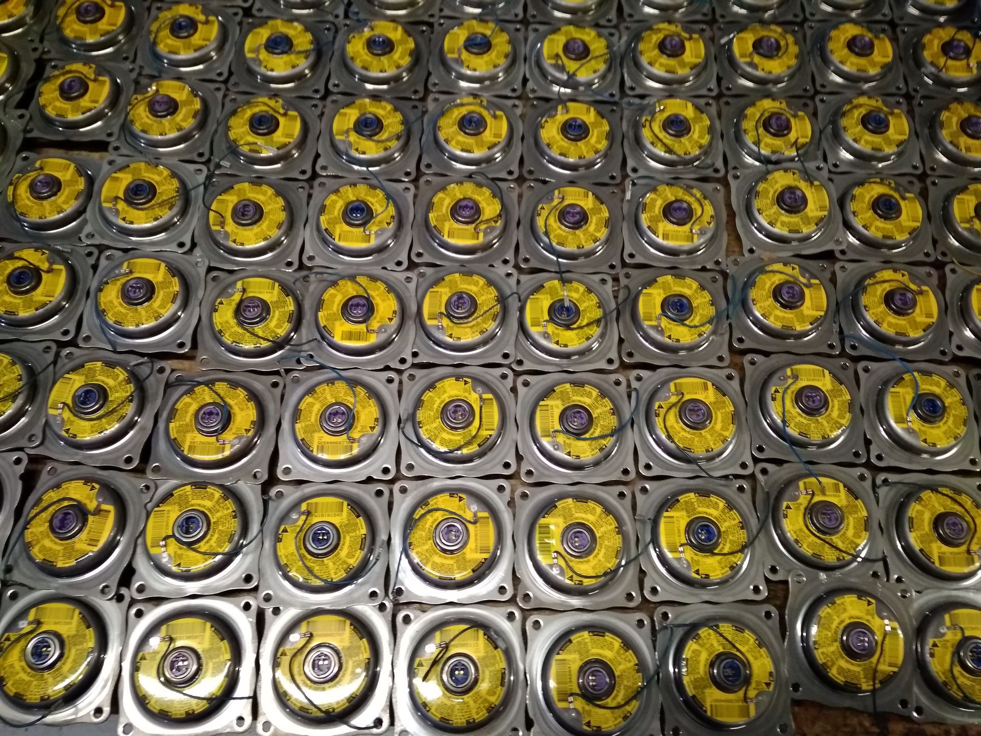 Conjunto de pequeños altavoces metálicos con centro amarillo dispuestos en forma de cuadrícula.