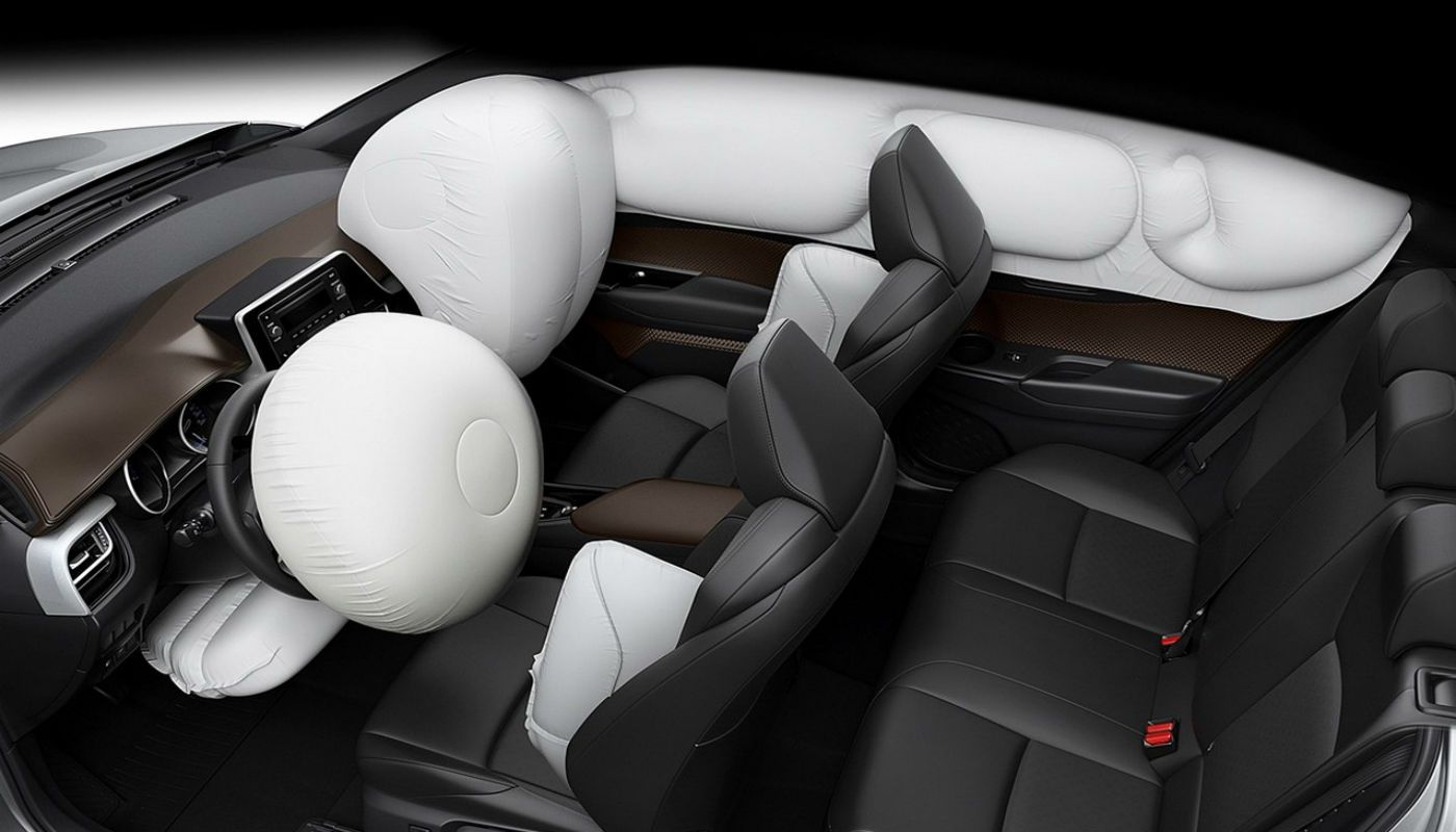 Vista interior del vehículo con airbags desplegados; airbags laterales, frontales y de techo visibles. Asientos negros y detalles en madera.