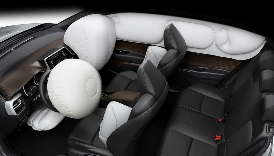 Vista interior del vehículo con airbags desplegados; airbags laterales, frontales y de techo visibles. Asientos negros y detalles en madera.