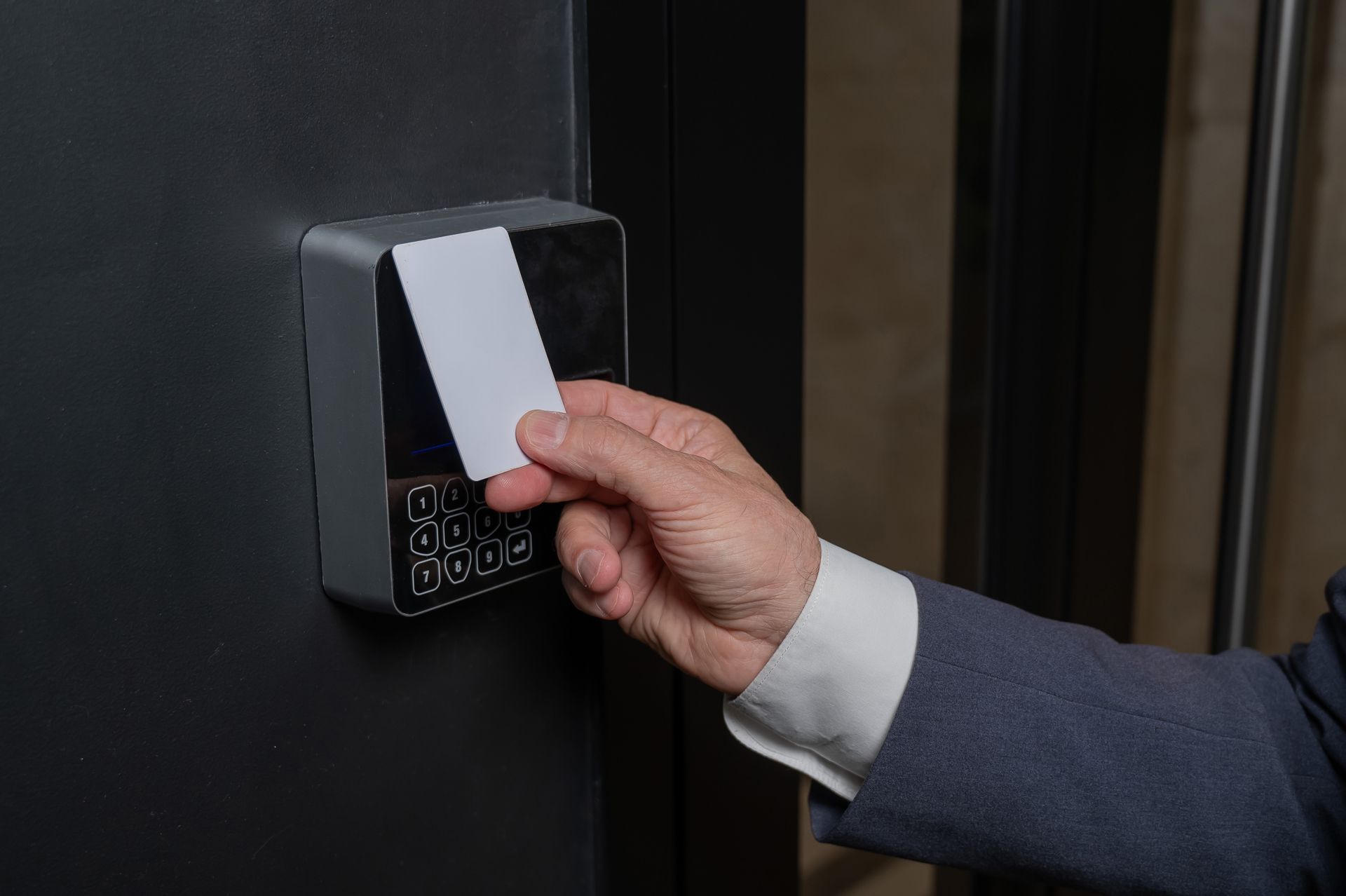 Hand inserting a card into a wall-mounted access reader near a door