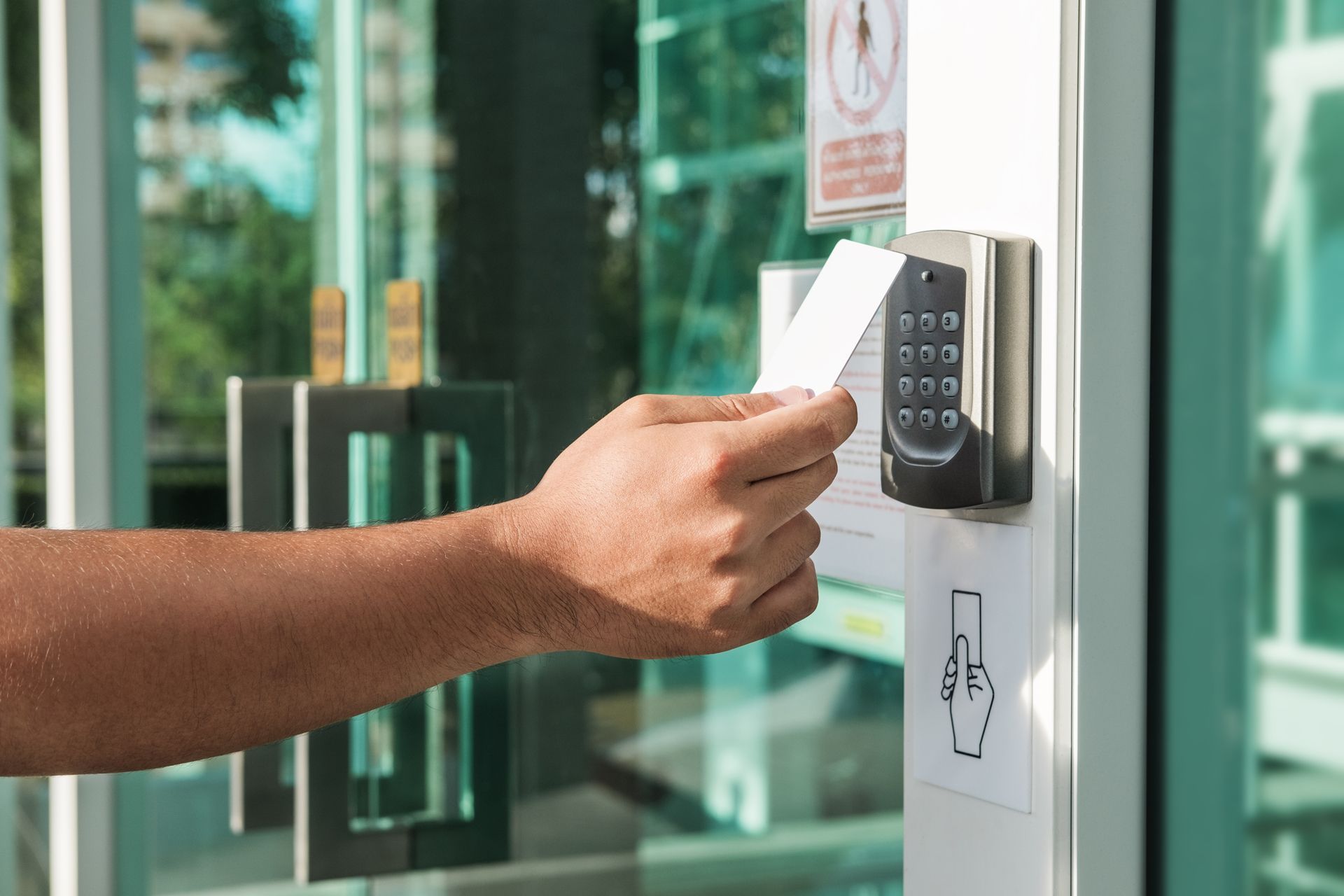 Hand entering a PIN on a keypad door lock at a glass entrance