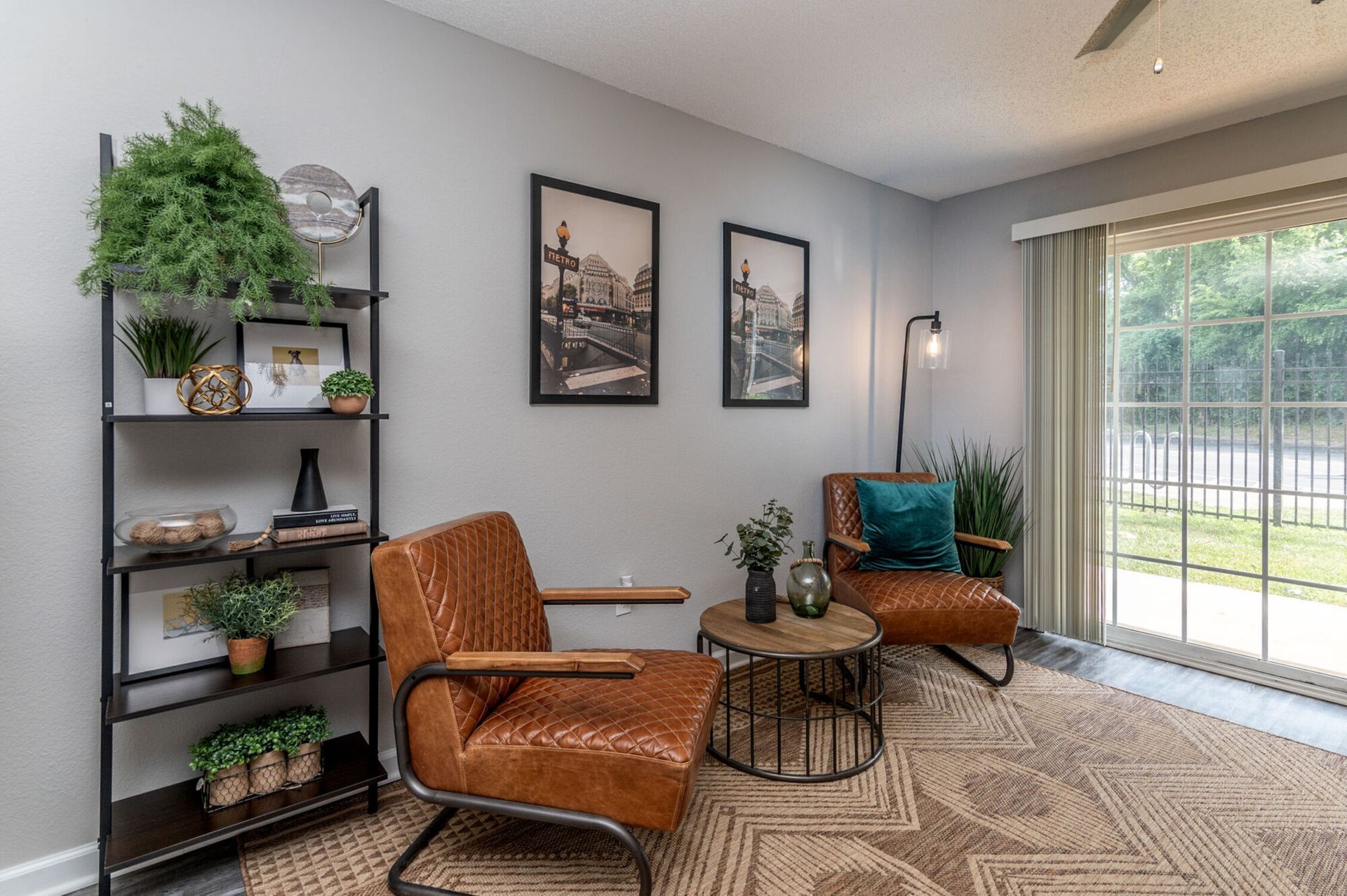 Living room with brown leather chairs, round table, shelves, artwork, and sliding glass door.