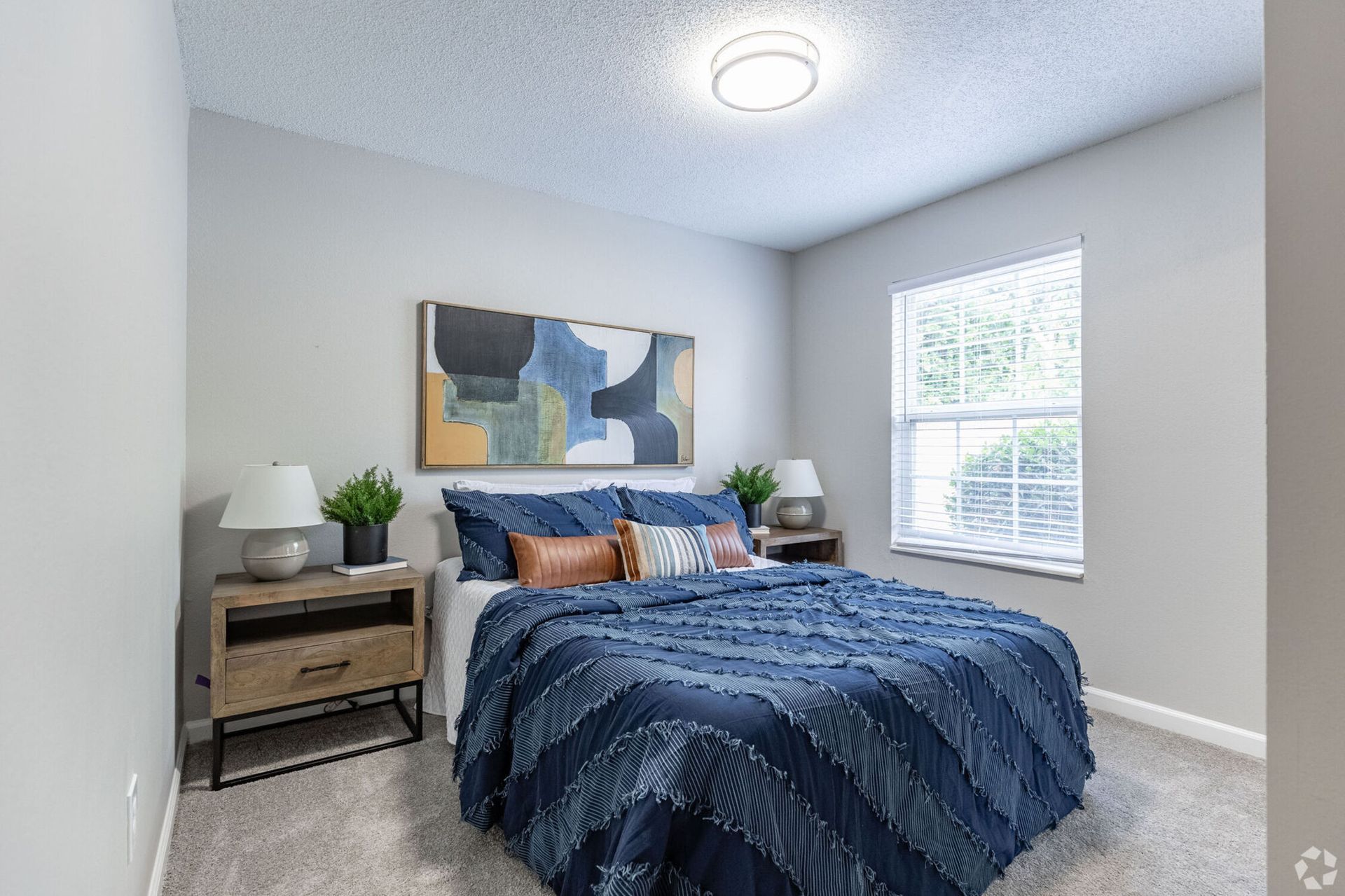 Bedroom with a bed covered in blue bedding, nightstands, artwork, and a window.