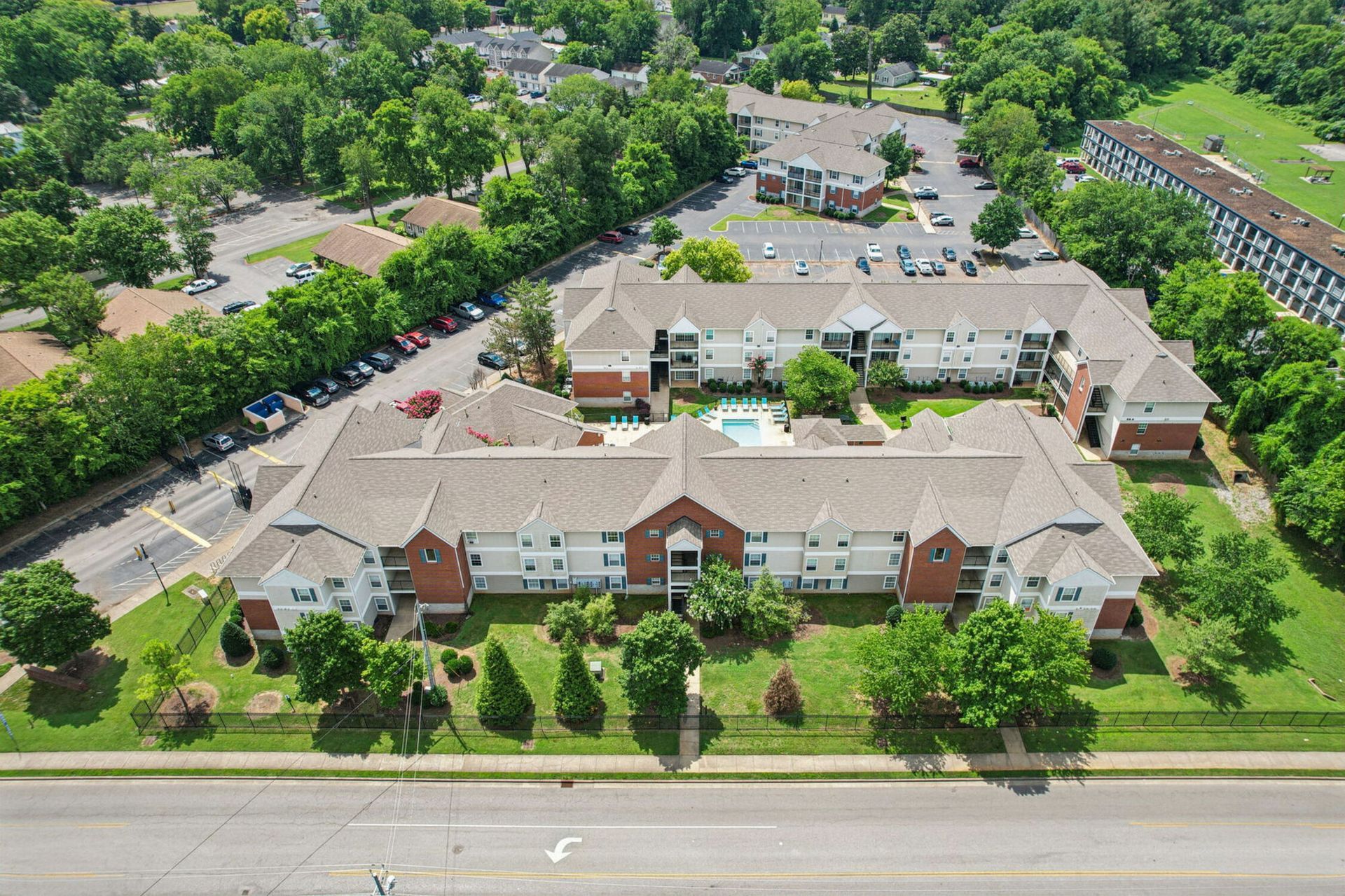 Aerial view of an apartment complex with red brick, white trim, and a pool in the courtyard surrounded by trees.