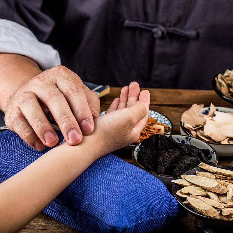 Person checking a child's pulse. Herbs in bowls sit nearby.