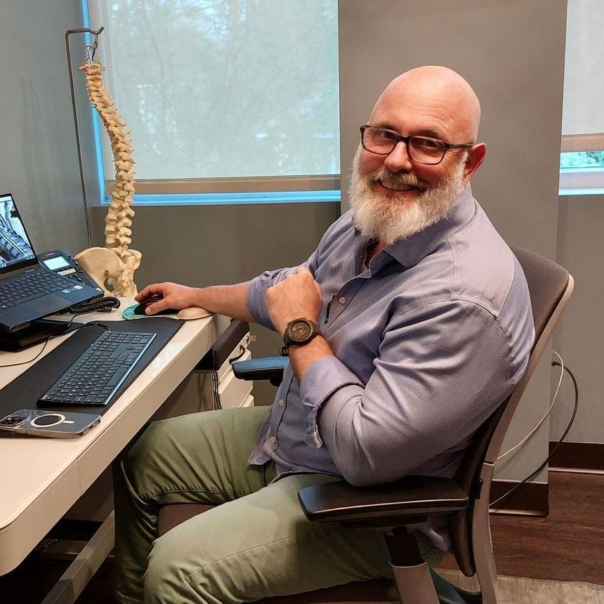 A man with a beard is sitting in front of a computer desk