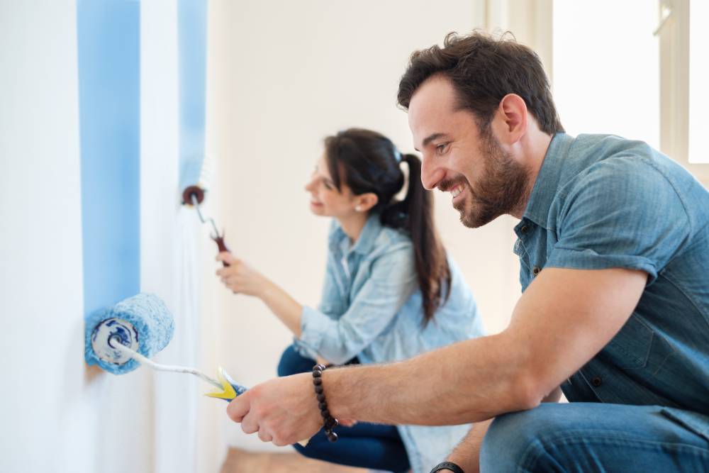 A man and woman use PPG Paint on rollers to paint walls of home