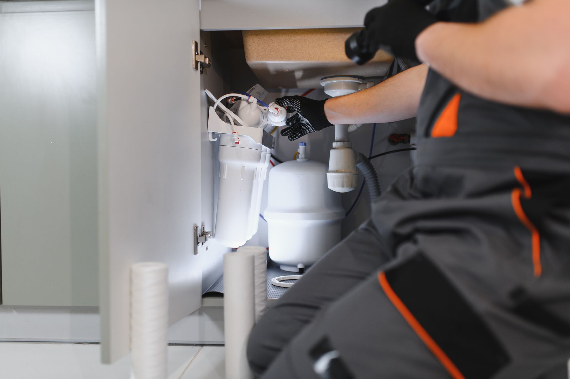 A plumber replacing white sediment filter cartridges in an under-sink water filtration system