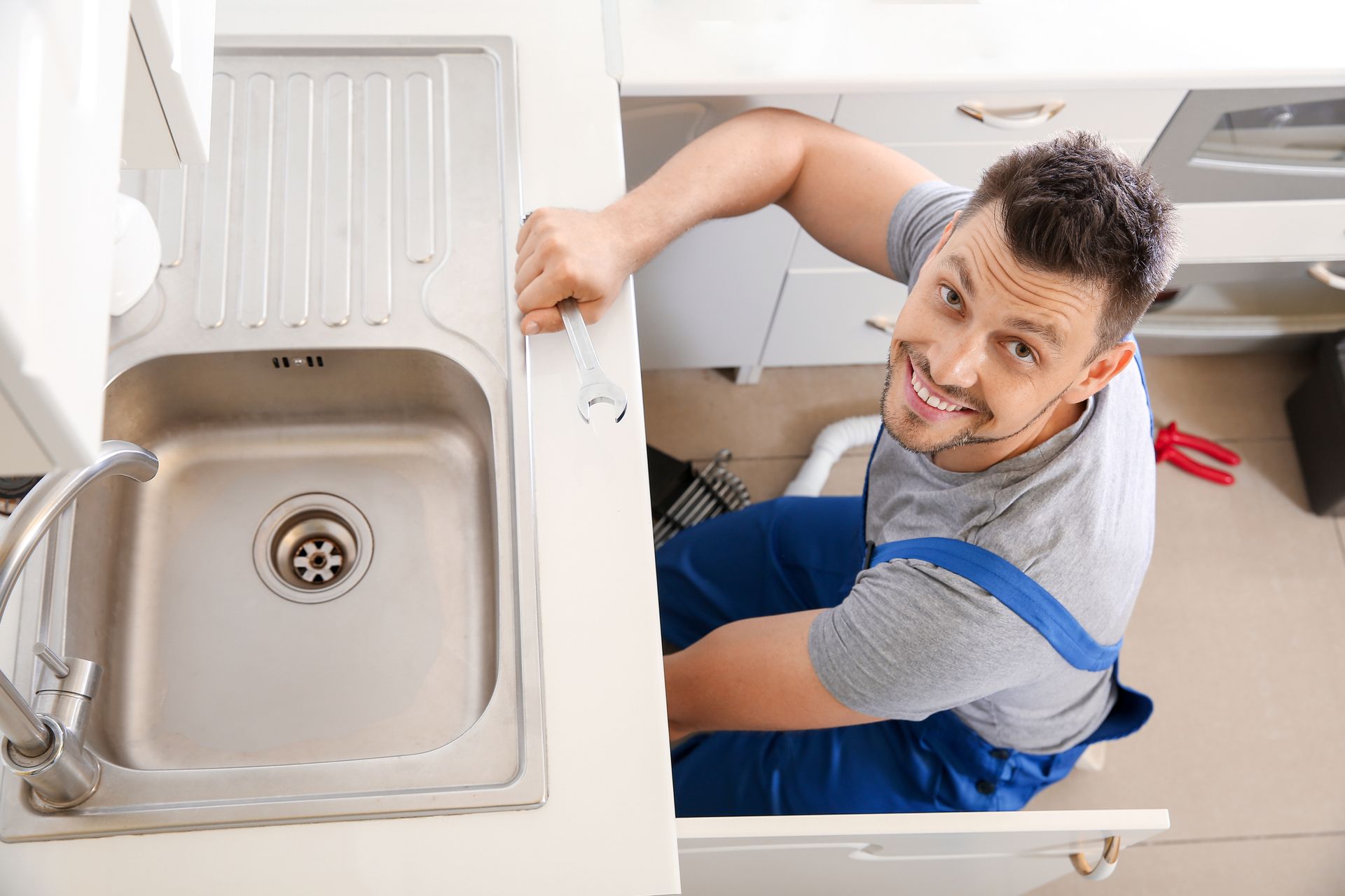 A professional home plumber smiling while fixing plumbing issues with the kitchen sink. A professional home plumber smiling while fixing plumbing issues with the kitchen sink.
