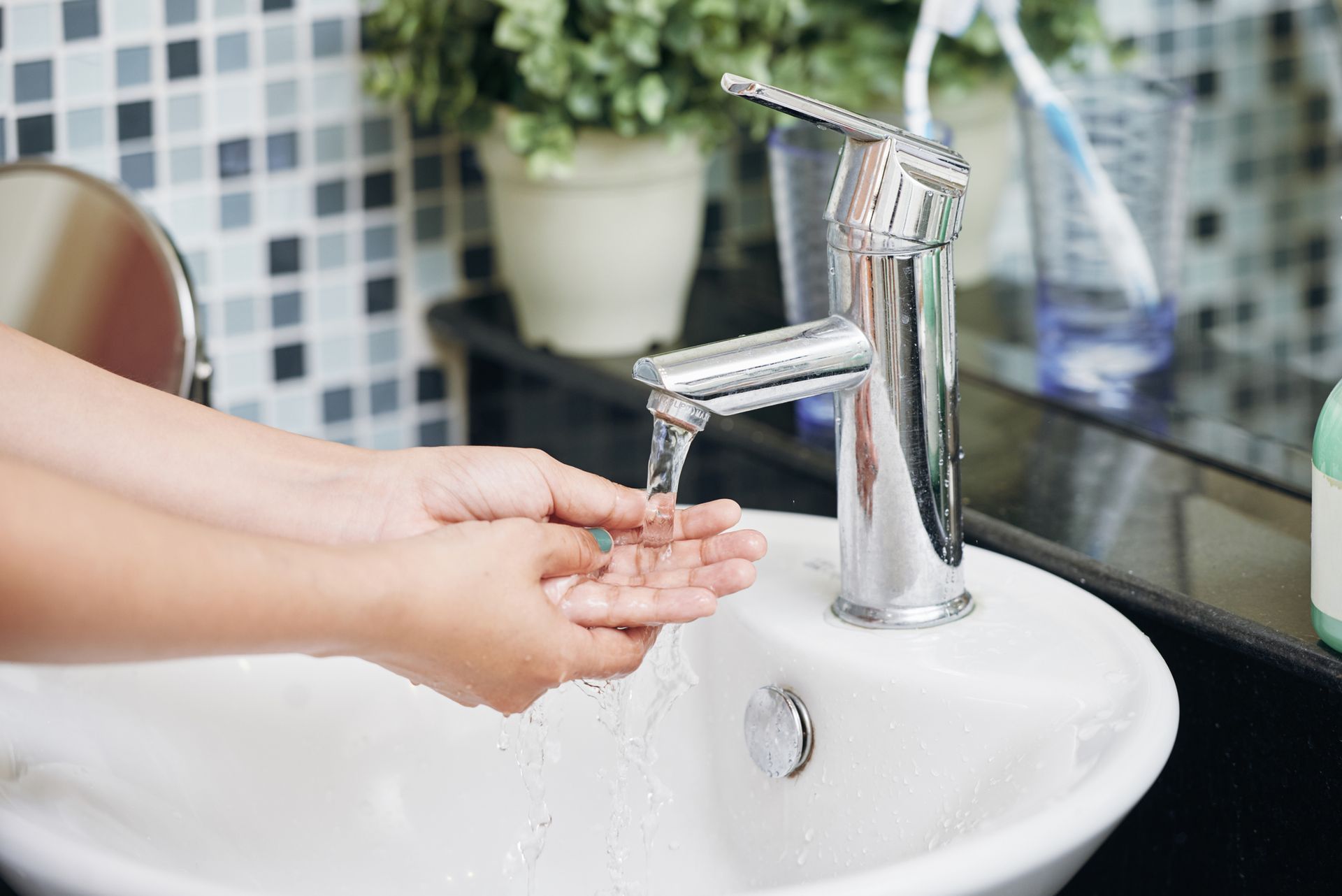 Person washing hands under running water in modern bathroom sink with chrome faucet hygiene care.
