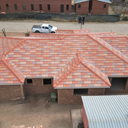 Brick homes with orange tiled roofs under construction. White truck parked nearby.