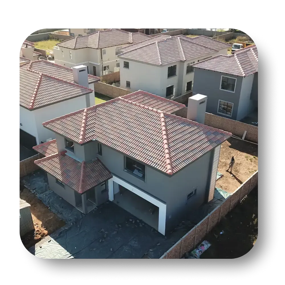 Aerial view of a newly constructed gray house with a terracotta tile roof, surrounded by other houses in a suburban setting.