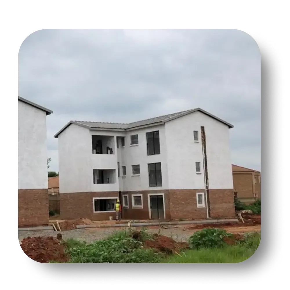 Three-story white apartment building under construction with brick base, against a cloudy sky.