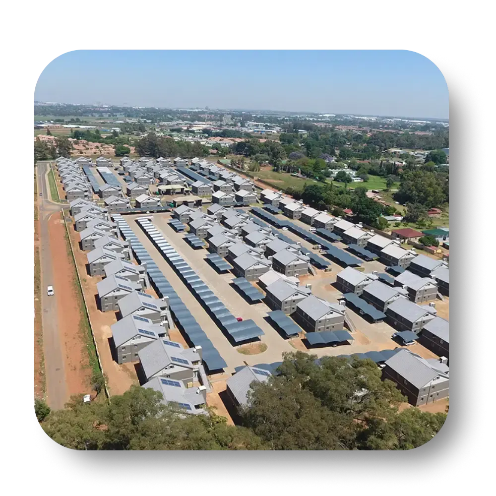 Aerial view of a housing complex with rows of homes and garages. Grey rooftops and blue skies.