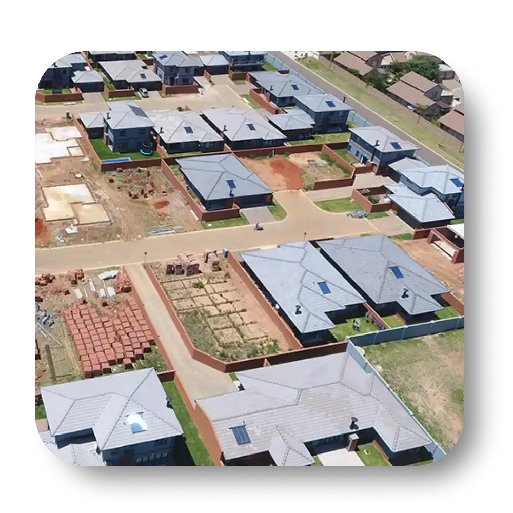 Aerial view of a suburban neighborhood under construction with multiple houses, red-brown roofs, and empty lots.