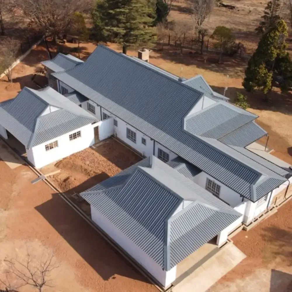 Aerial view of a white building with a gray roof, surrounded by dry earth and trees.