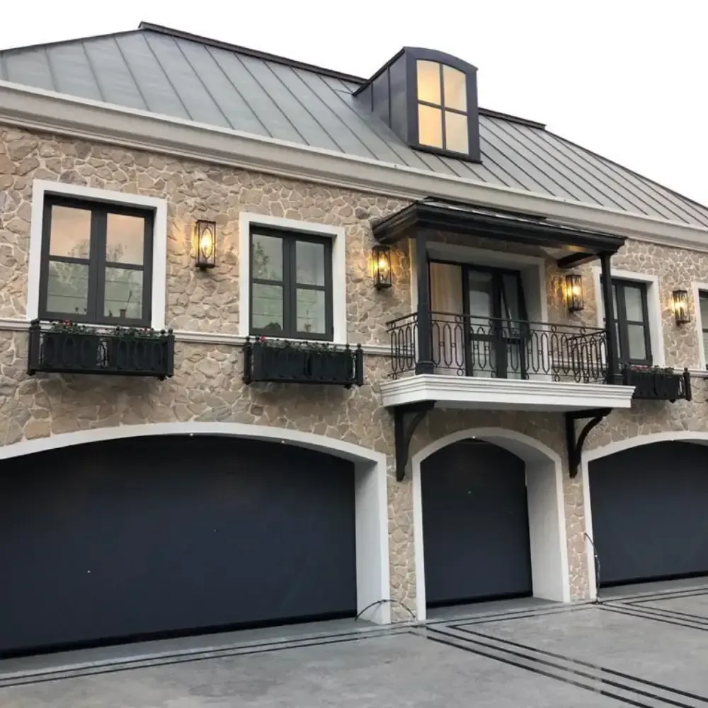 Stone facade with three black garage doors, balcony, windows, and metal roof.