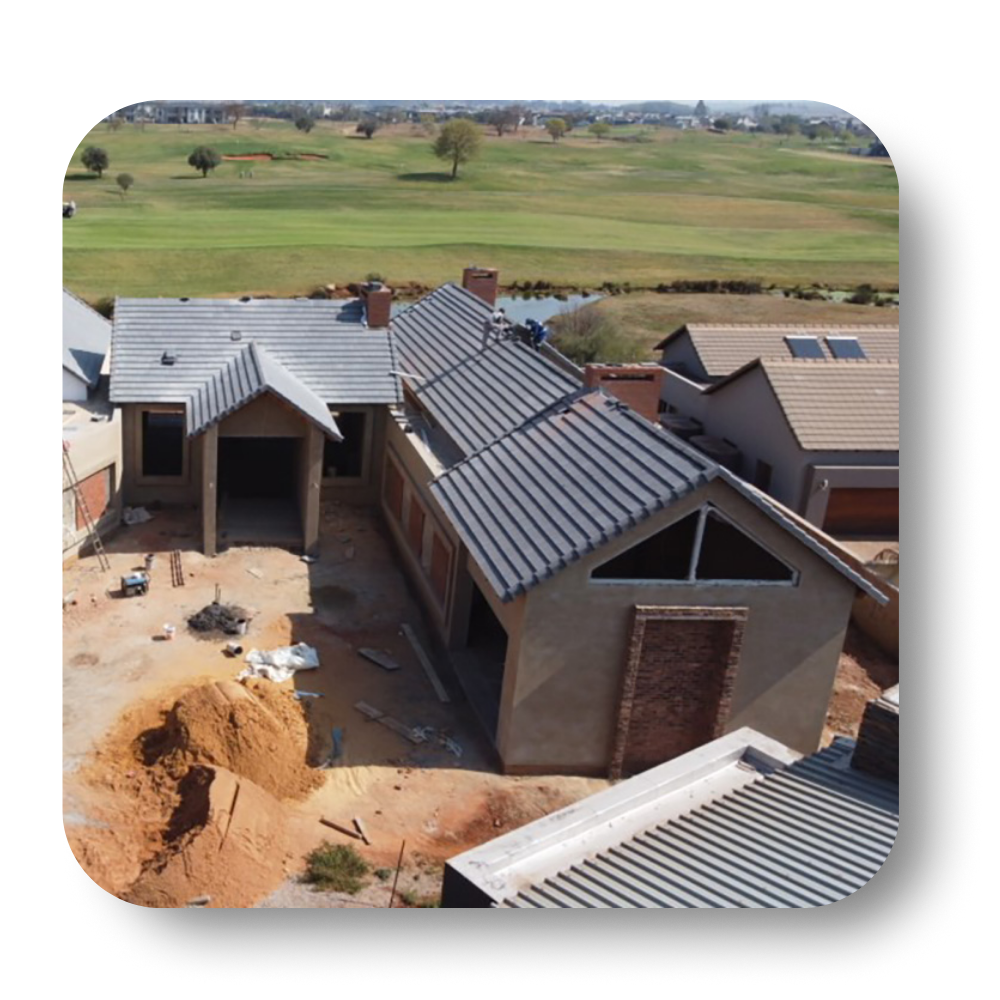 Construction site with unfinished house, gray tile roof, brick and tan walls, overlooking green golf course.