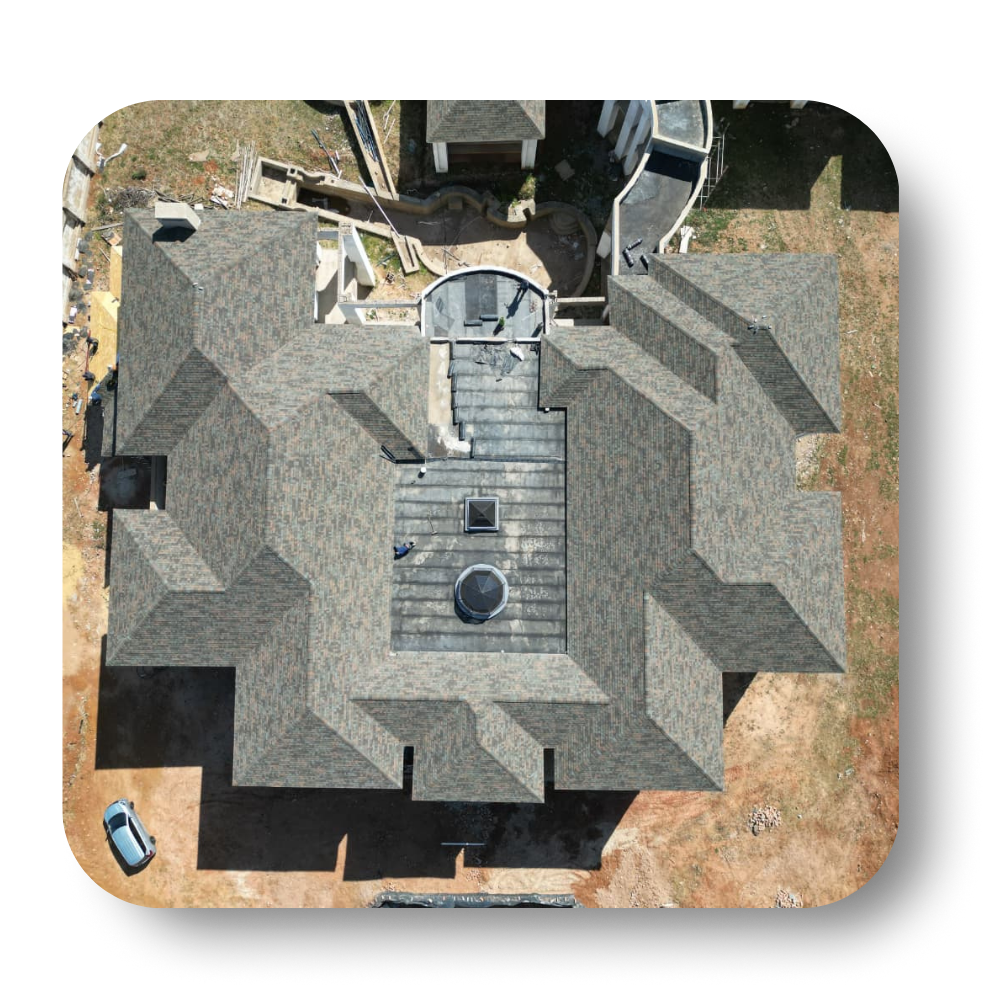 Overhead view of a complex, multi-sectioned, gray-roofed house surrounded by dirt and a parked car.