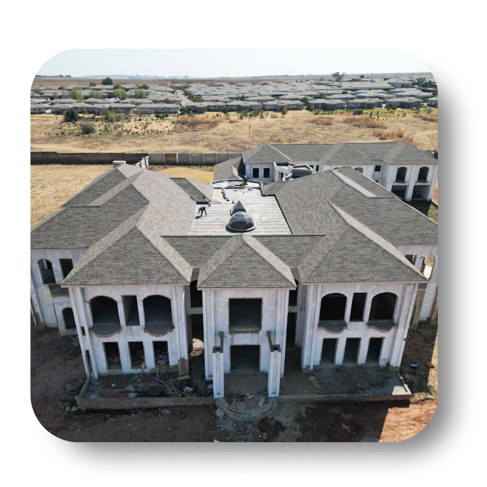 Unfinished multi-section mansion with gray roof, set on a dusty, undeveloped lot.
