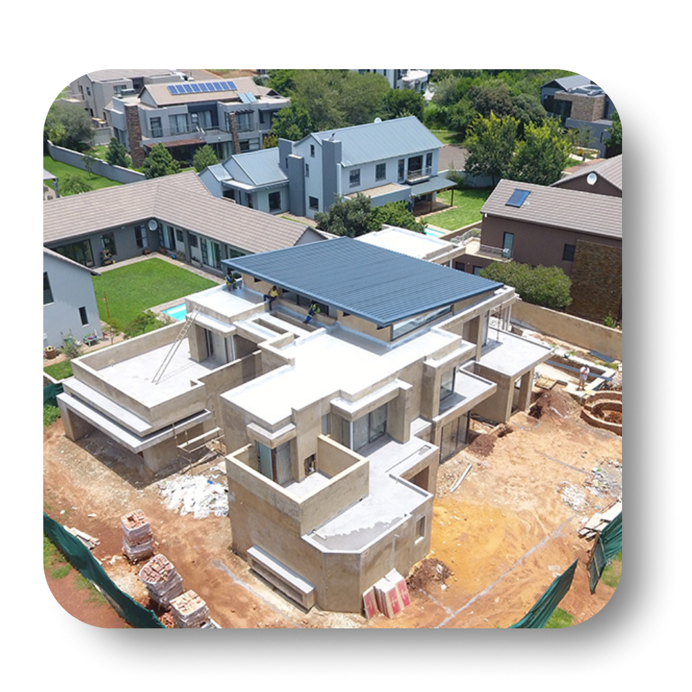 Aerial view of a modern home under construction with solar panels installed. Other houses and greenery are visible.