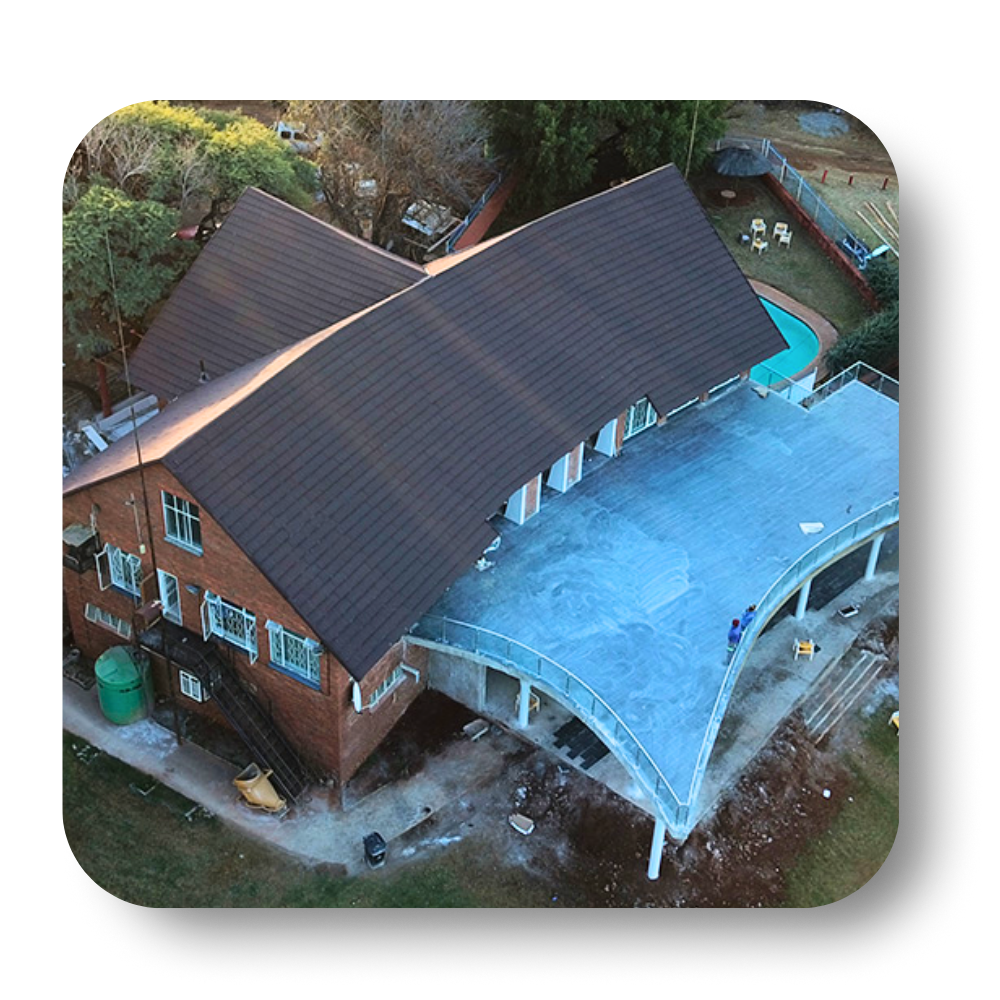 Aerial view of a brick building with a brown roof, a flat blue patio, and a pool.