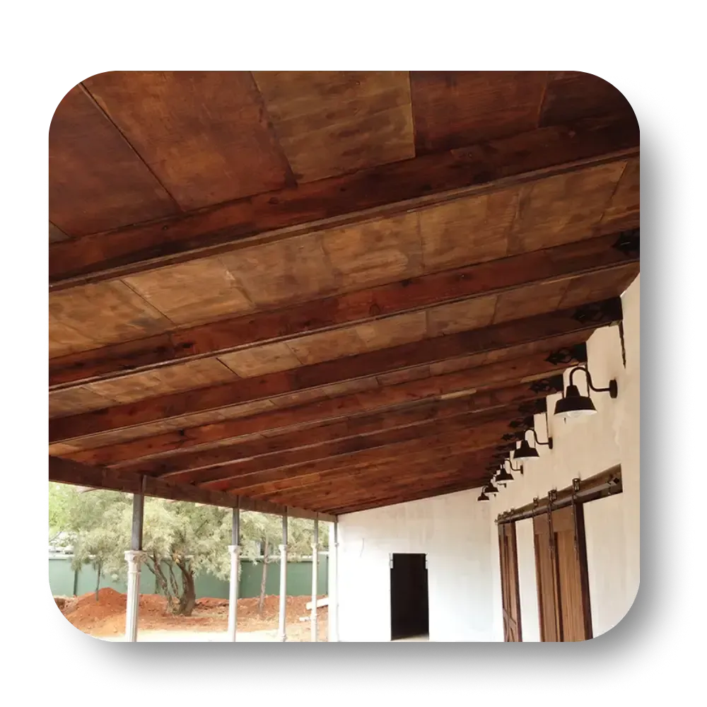 Wooden porch ceiling with beams, attached to a white building with black sconce lights.