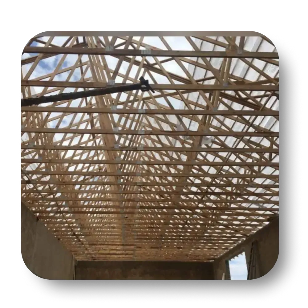 Wooden roof trusses inside a building frame against a cloudy sky.